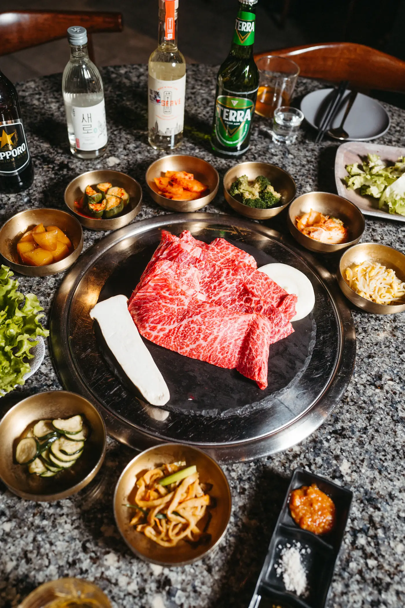 Marbled slices of raw beef on a round grill surrounded by banchan