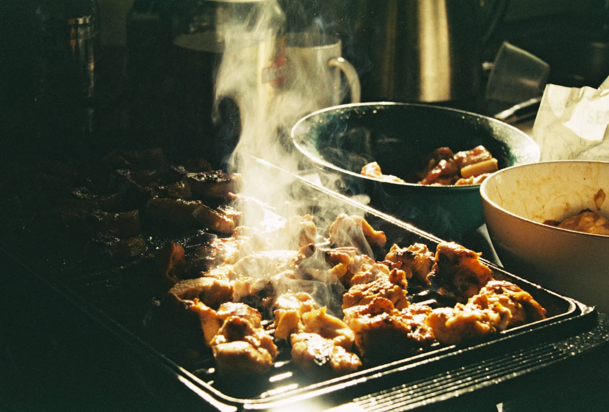Chicken pieces smoking on a tabletop grill in a dark room