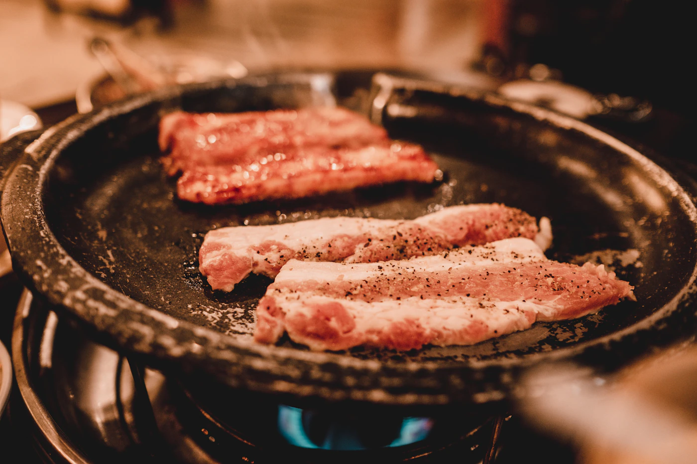 Strips of pork belly cooking on a round grill plate over a gas flame