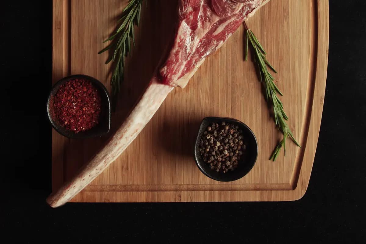 A dry-aged tomahawk steak on a wooden board with rosemary and coarse salt