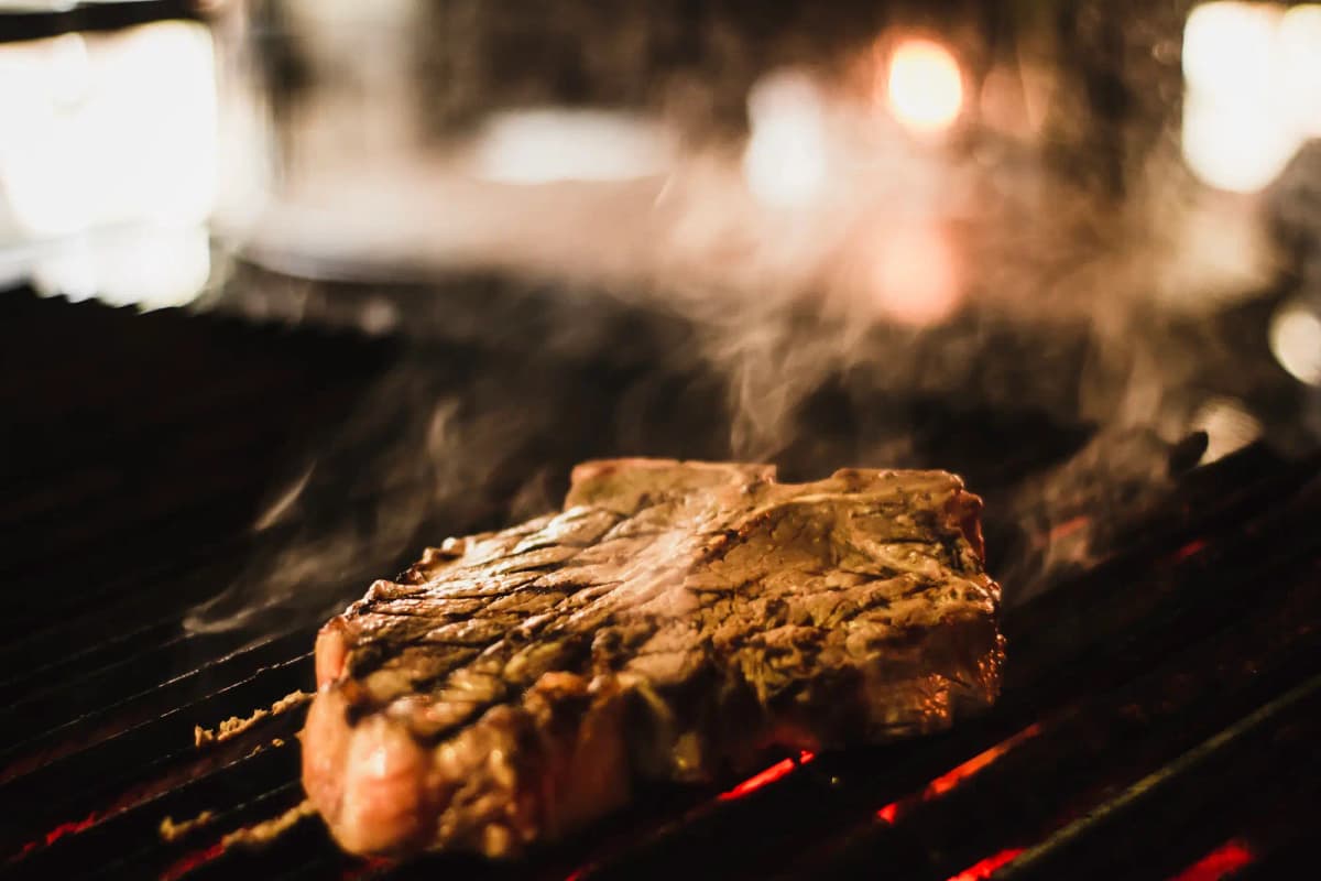 A thick steak searing on a charcoal grill, coals glowing red beneath it