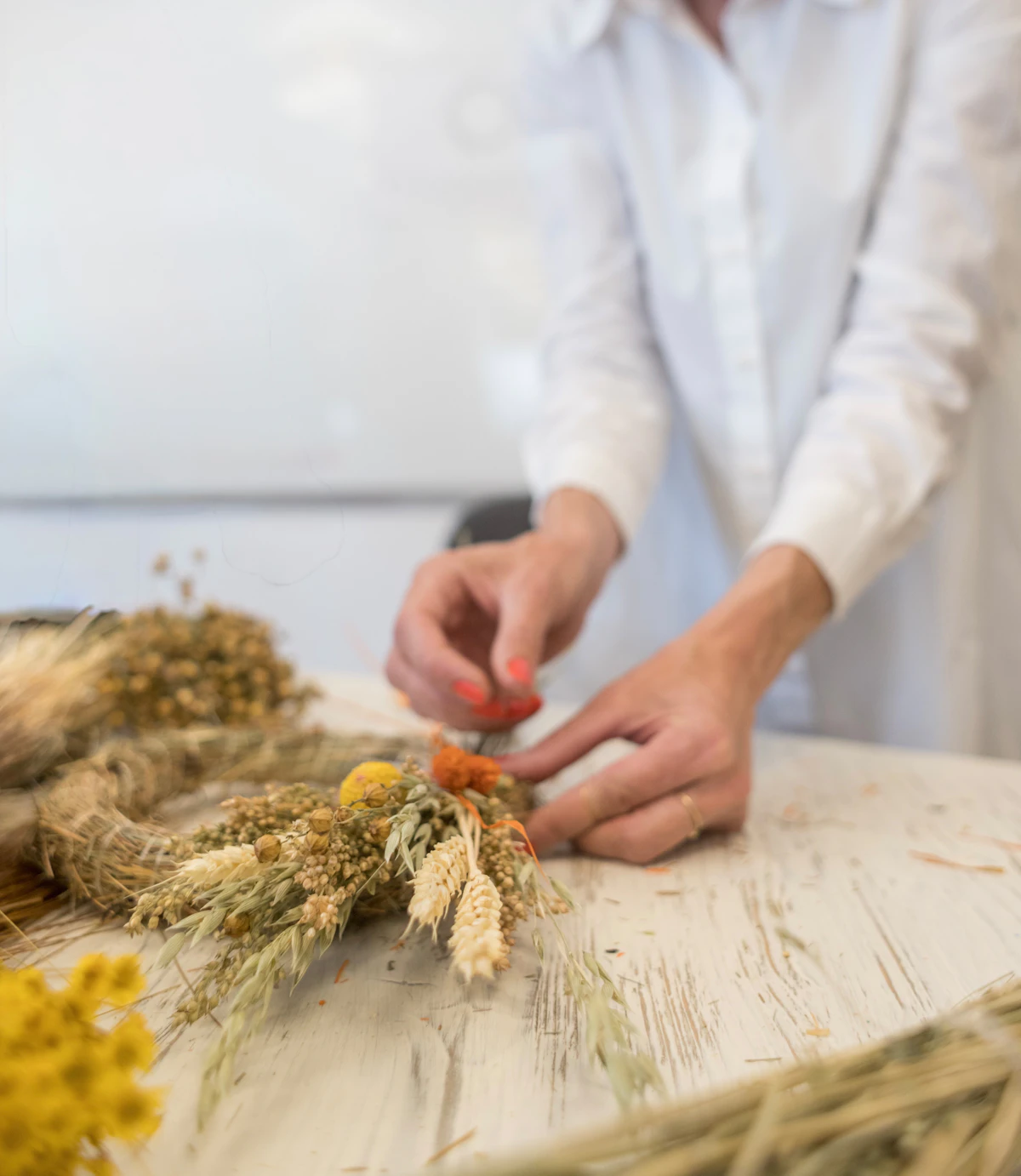 Hands wiring dried flowers onto a wreath at a wooden table