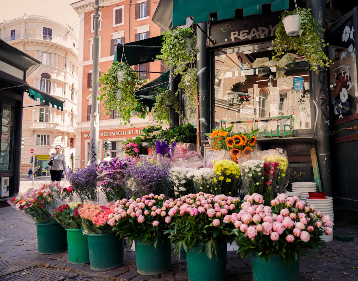 A flower kiosk on a city sidewalk with buckets of pink, purple and yellow flowers out front