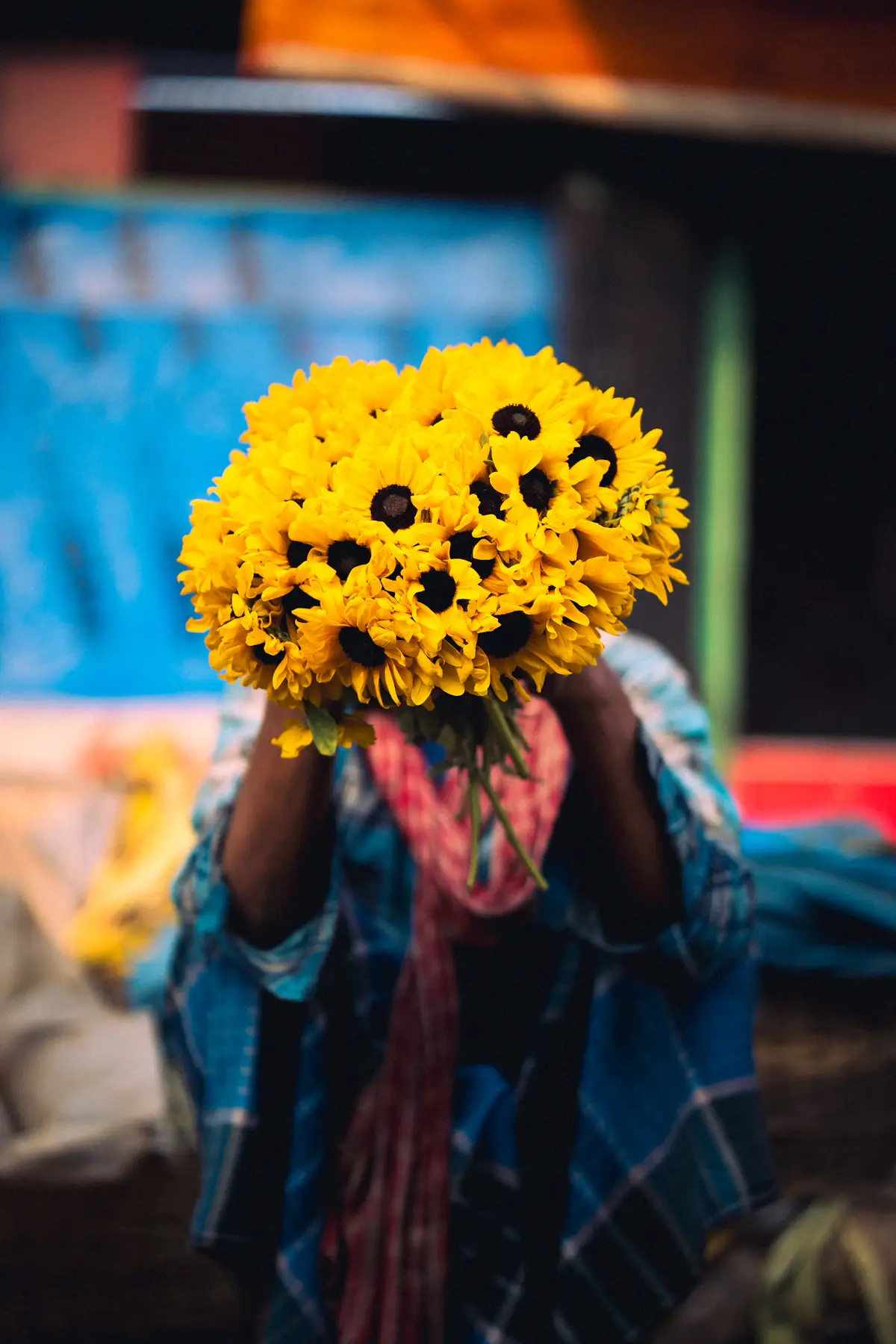 A person holding a big bunch of yellow sunflowers in front of their face