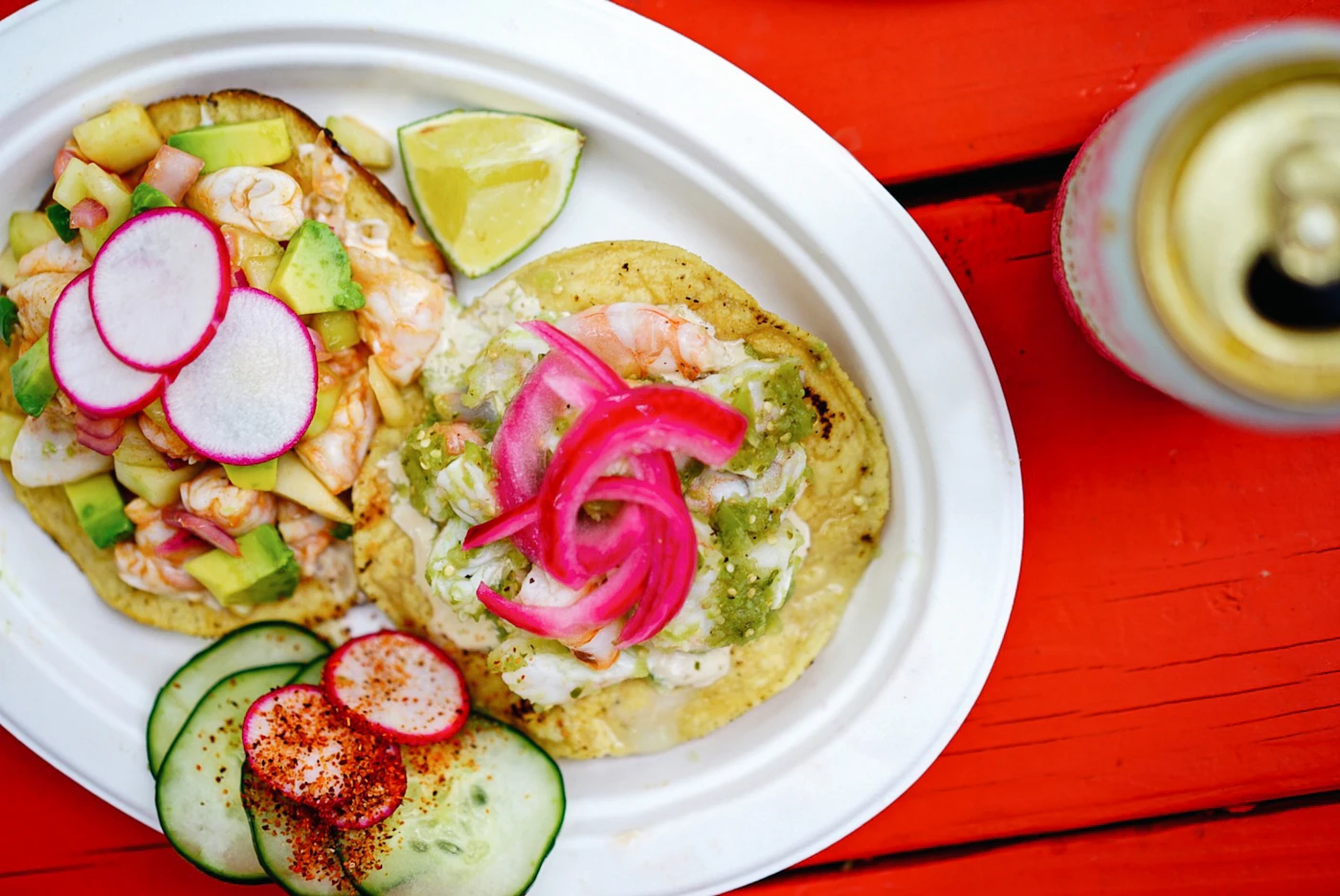 Two tostadas topped with shrimp ceviche, avocado, radish and pink pickled onion on a red table