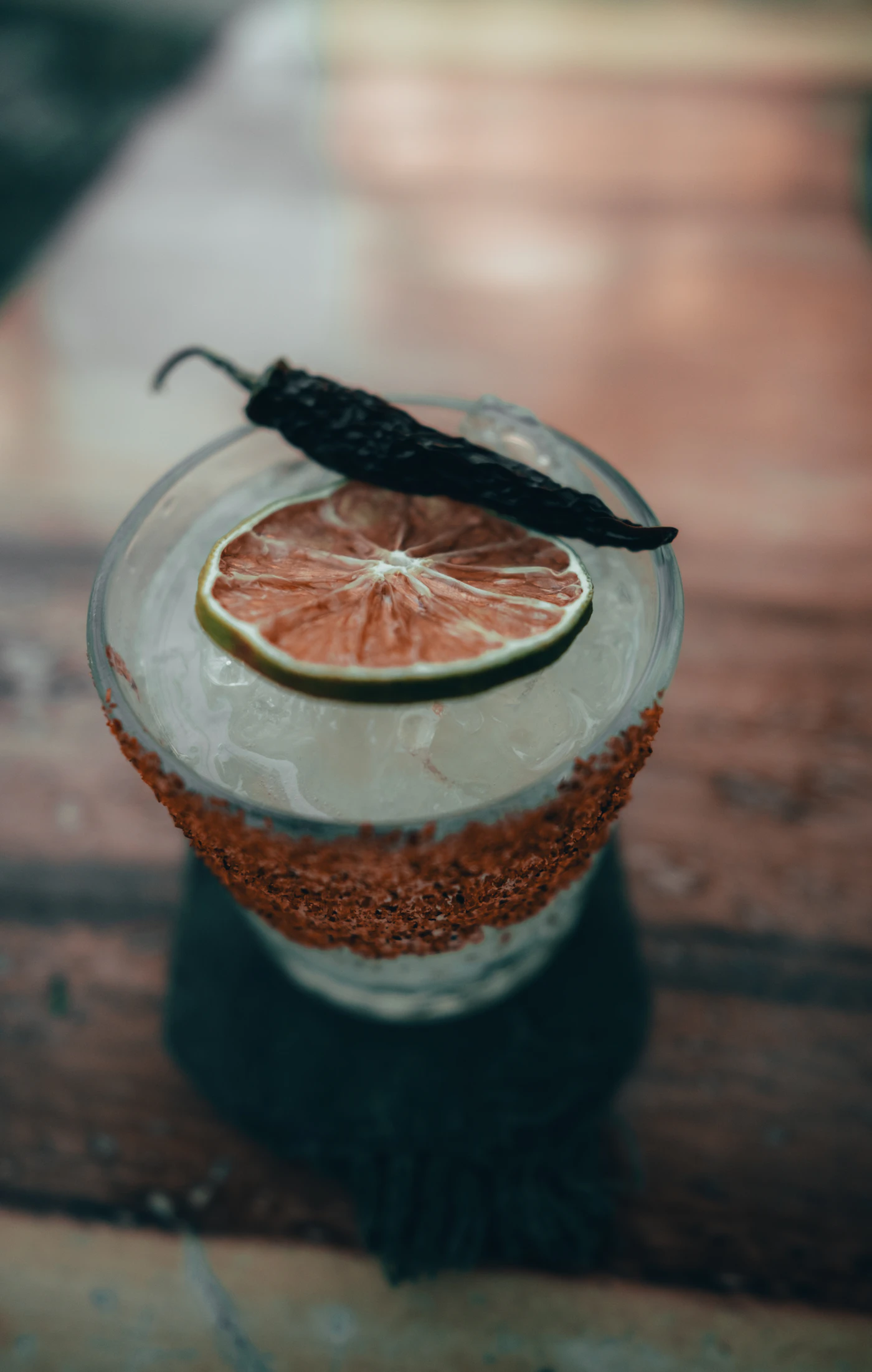 A glass of mezcal over ice with a dried orange slice and a rim of chile salt