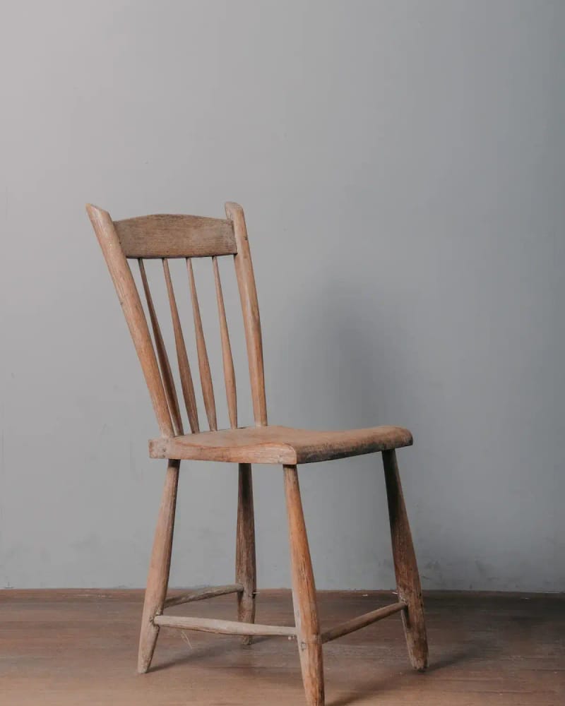 The Bryne dining chair, a spindle-back chair in oiled oak, against a grey wall