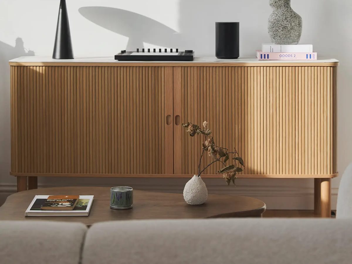 A low fluted-oak sideboard with a lamp, ceramics and a single branch in a vase