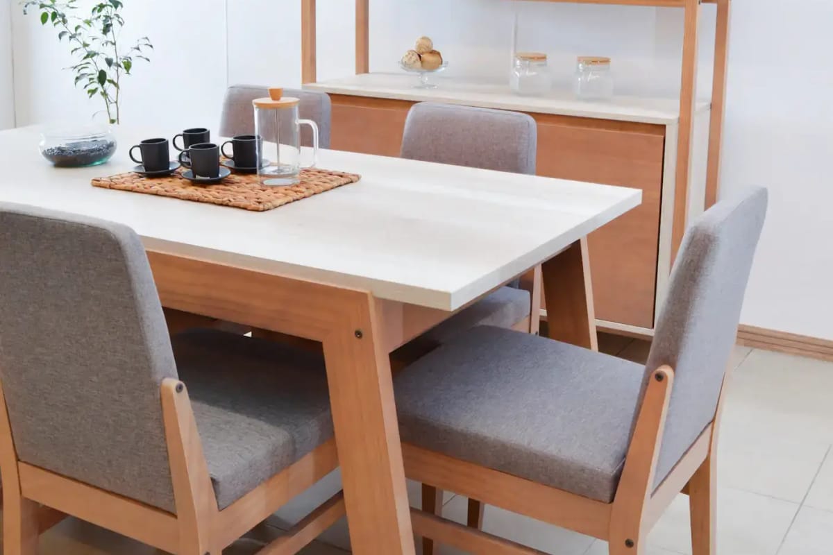 A pale oak dining table set with a tray of cups, grey upholstered chairs around it