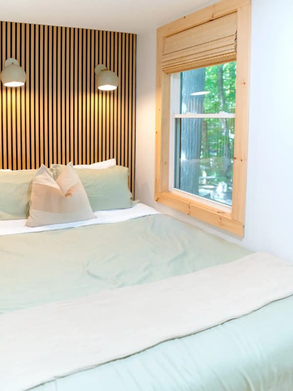A bed with sage green bedding against a slatted wood wall