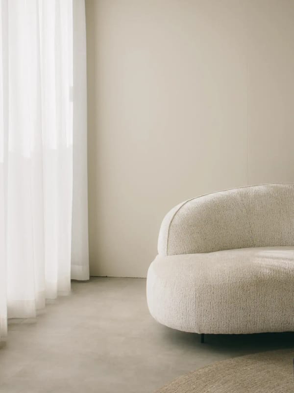 A rounded bouclé armchair beside sheer curtains