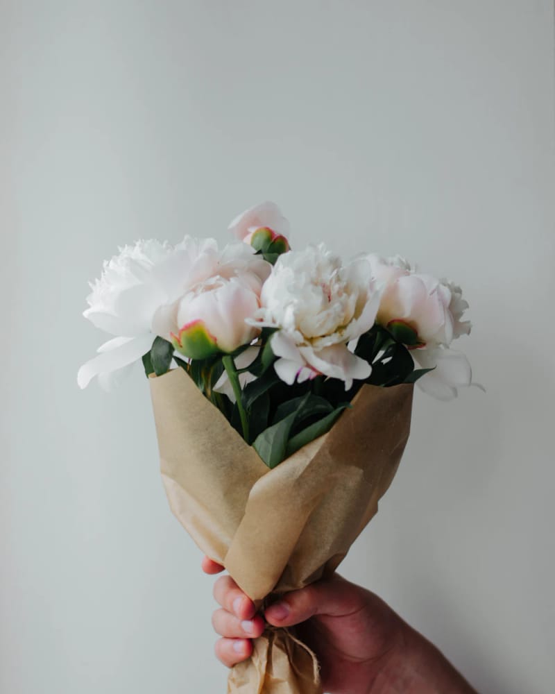 A hand holding white peonies wrapped in brown paper