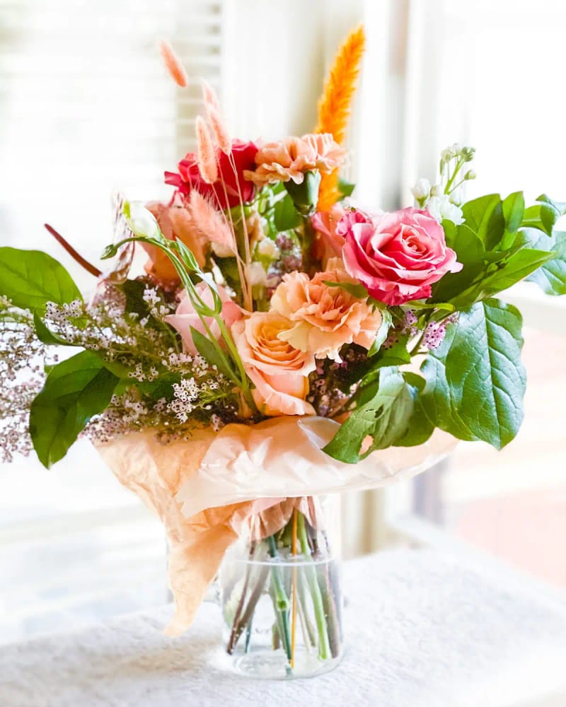 A bouquet of pink and peach roses in a glass vase by a sunny window