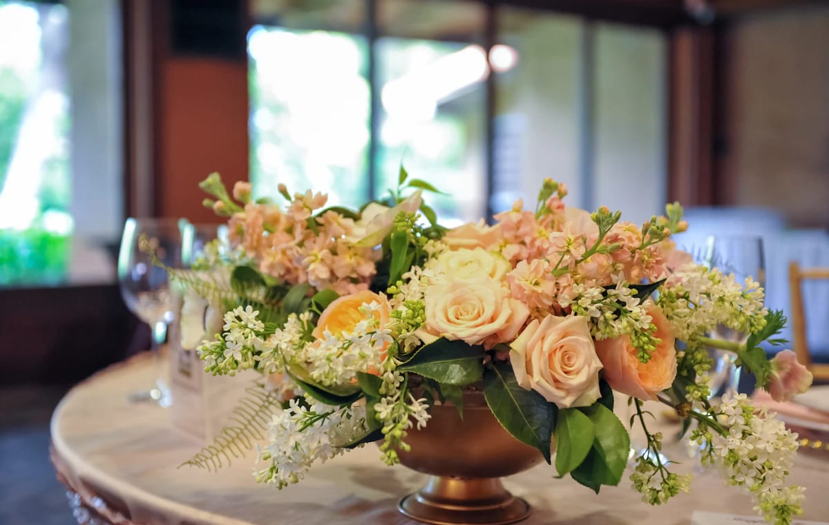 A low centerpiece of peach roses and greenery in a copper bowl on a reception table