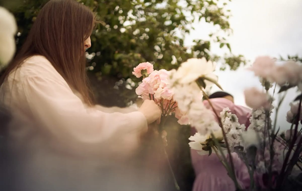A florist in a cream blouse arranging pale pink carnations in a garden