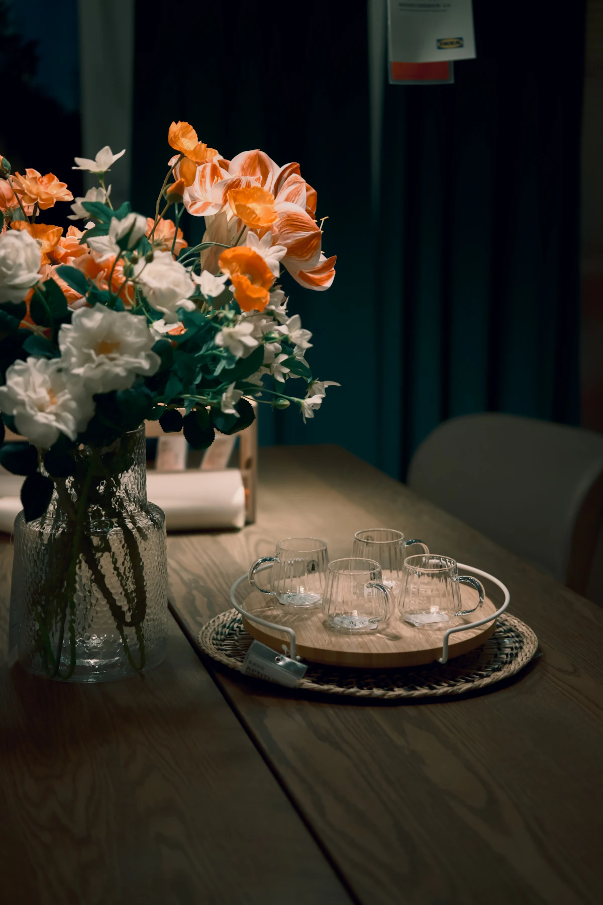 A glass vase of white and orange flowers on a wooden table set with teacups