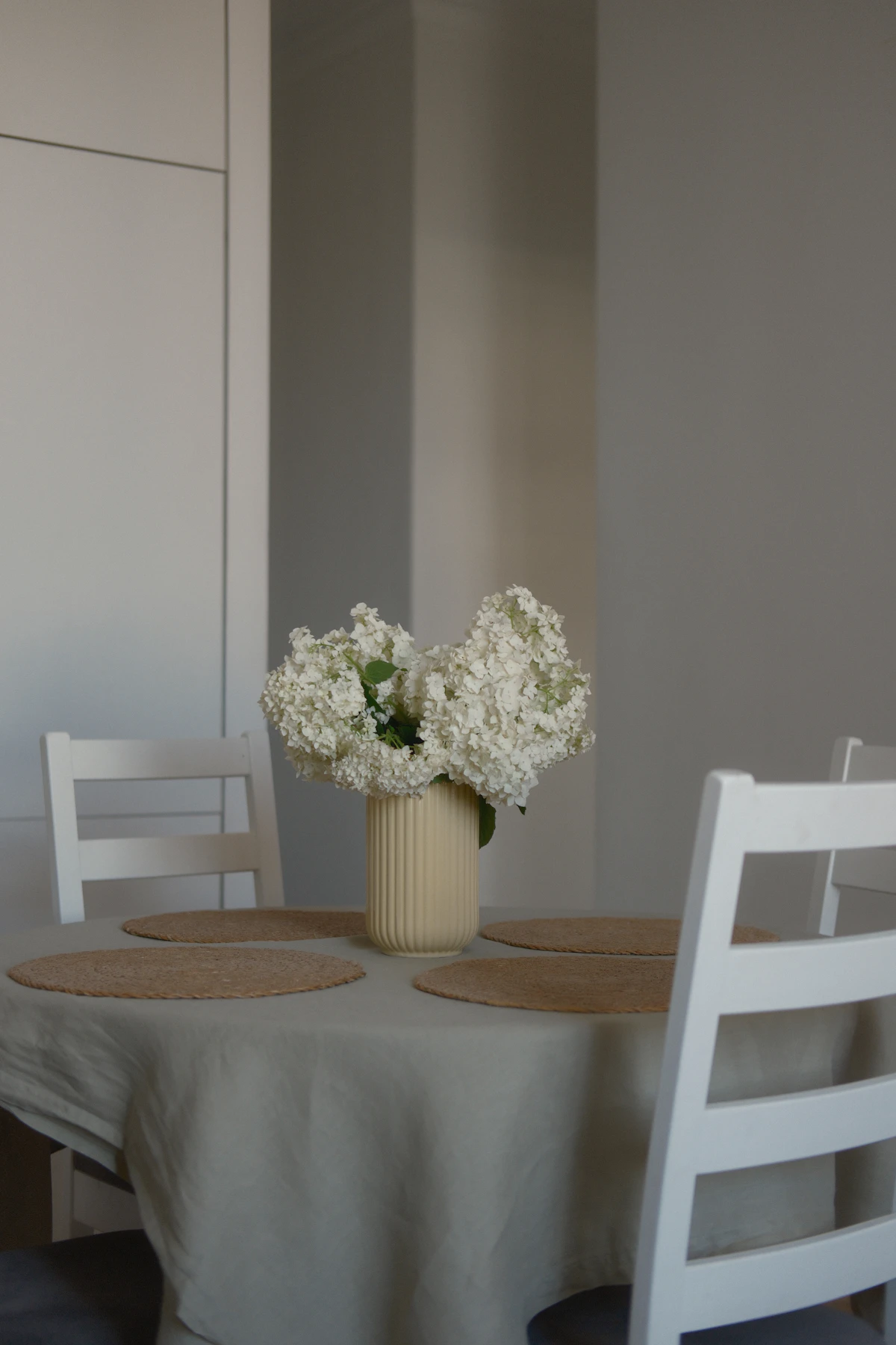 White hydrangea in a ribbed cream vase on a dining table