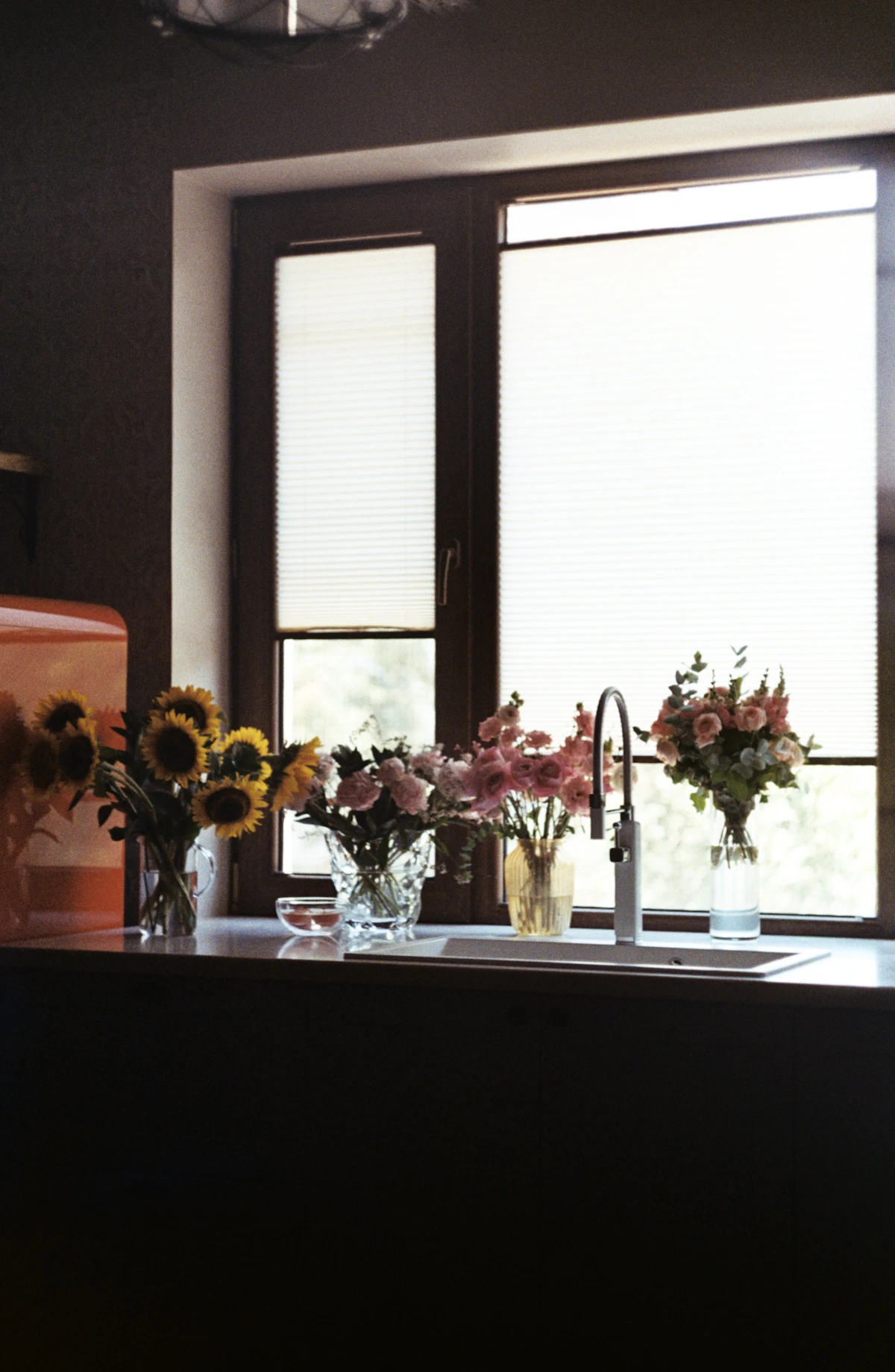 Sunflowers and pink flowers in jars on a kitchen counter by a sunny window