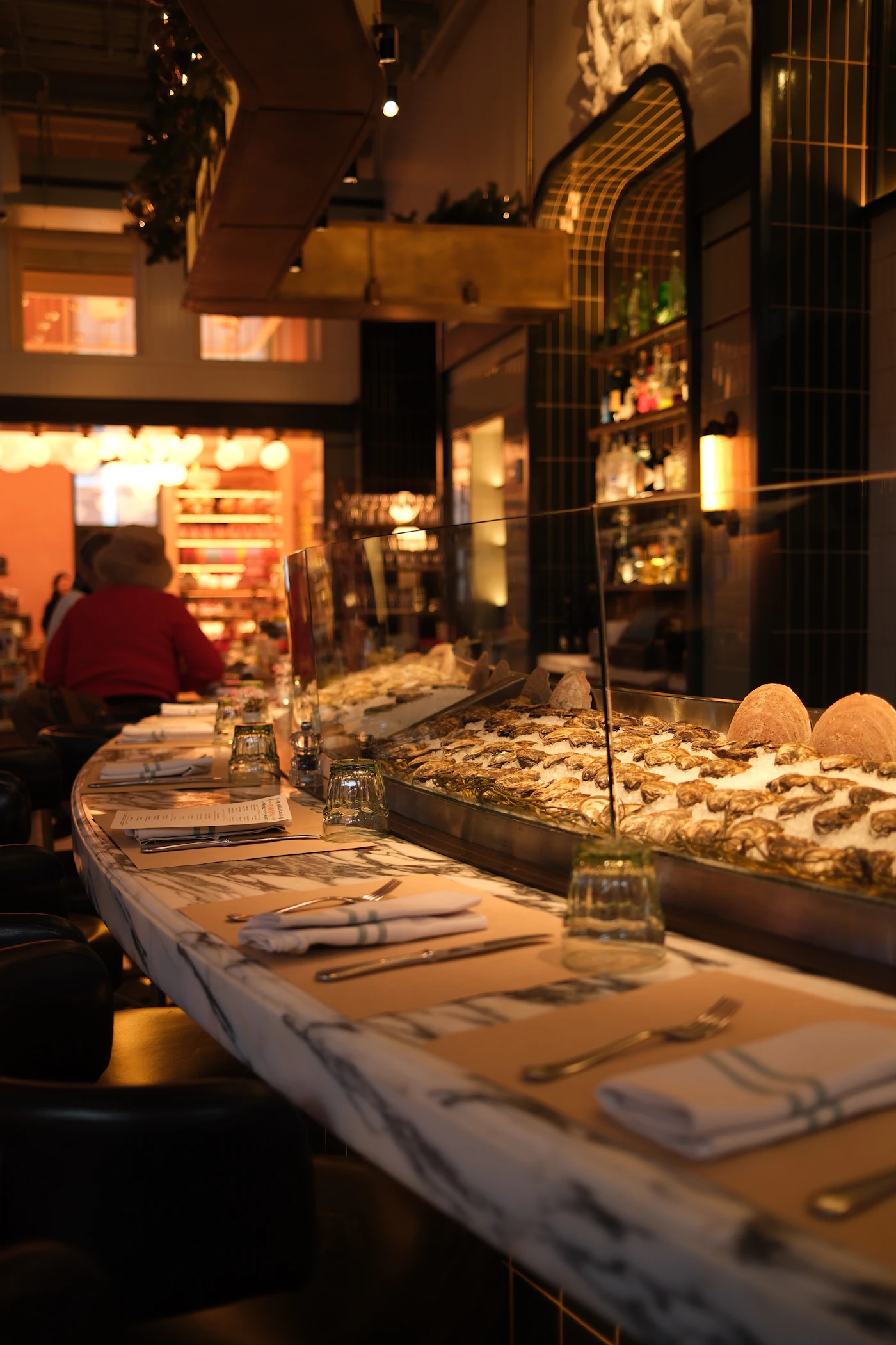 The raw bar at night: oysters on ice behind the glass, place settings along the counter
