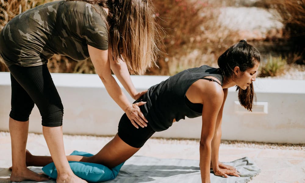 A teacher adjusting a student's plank pose on a mat outdoors