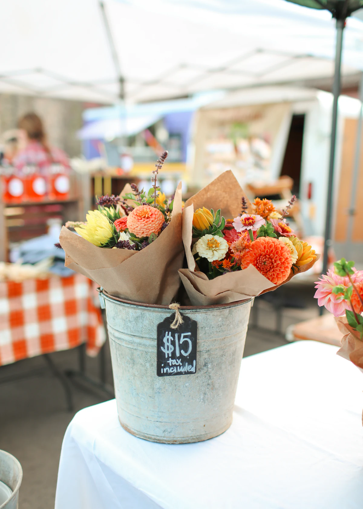 Paper-wrapped bunches of orange and peach dahlias in a metal bucket with a chalk price tag