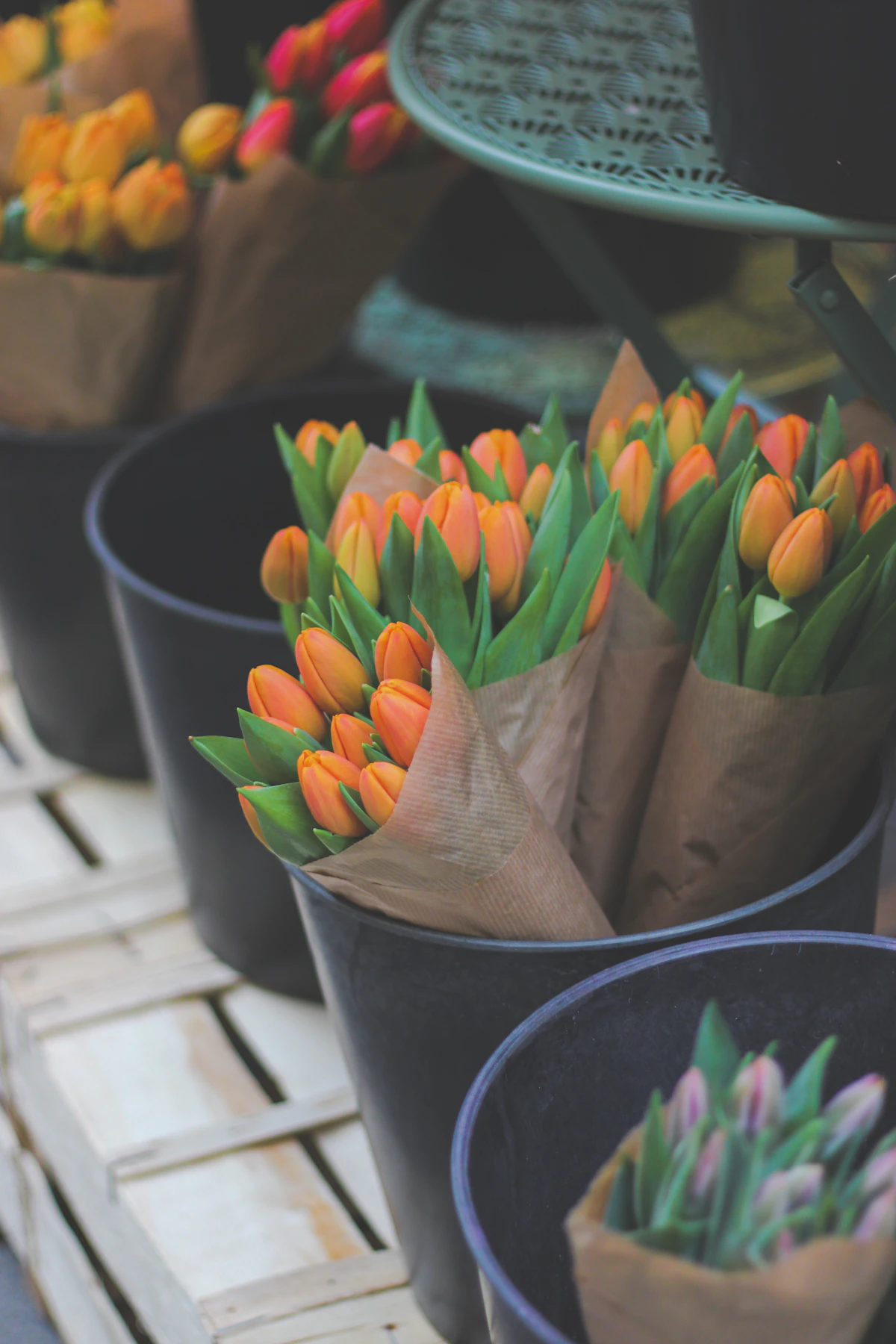Orange tulips wrapped in brown paper standing in dark buckets