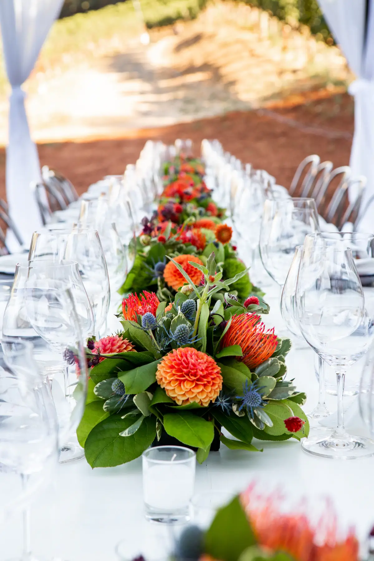 Orange dahlias and blue thistles running down a long table set with glasses