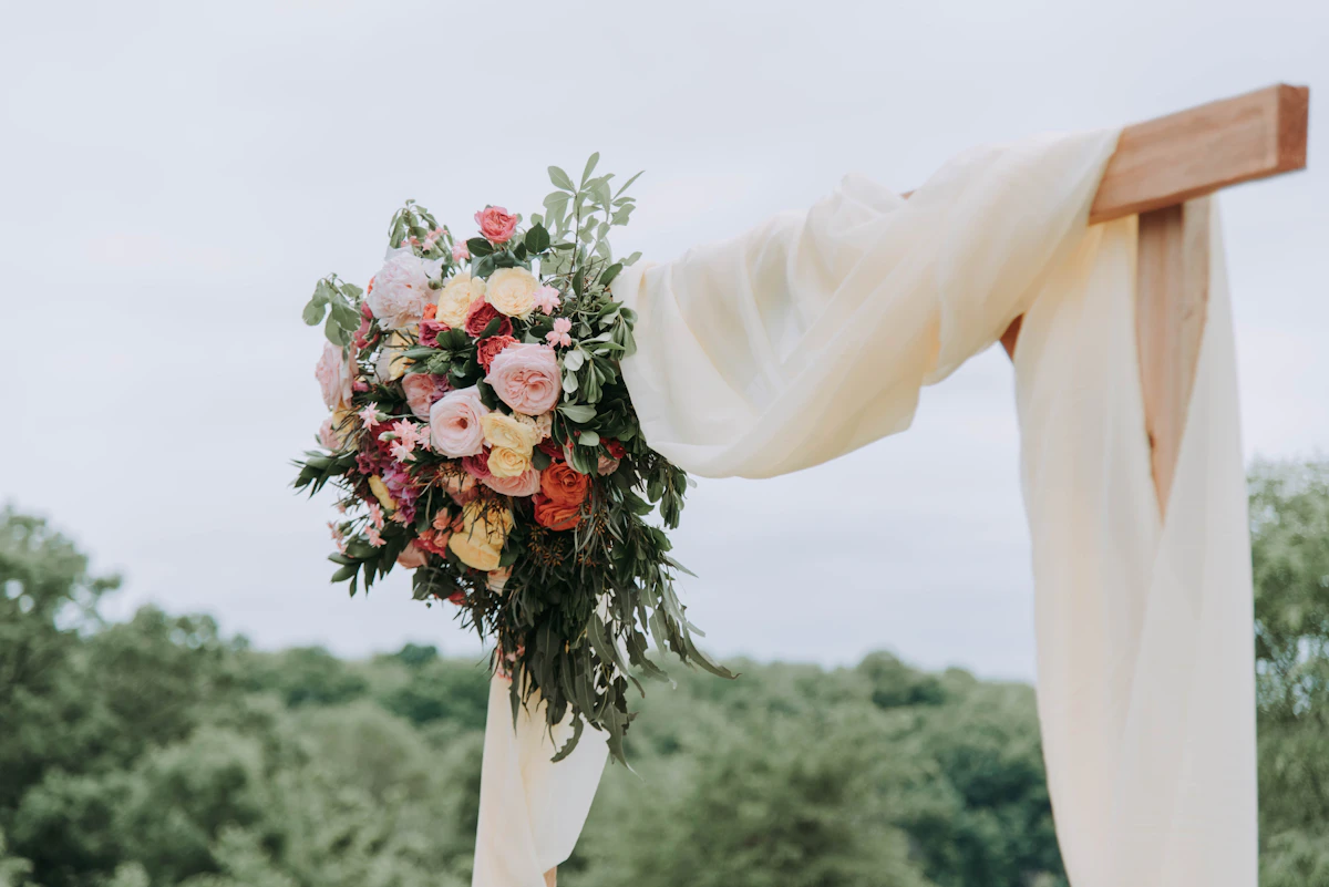 Blush and peach flowers tied to the corner of a wooden ceremony arch draped in ivory fabric