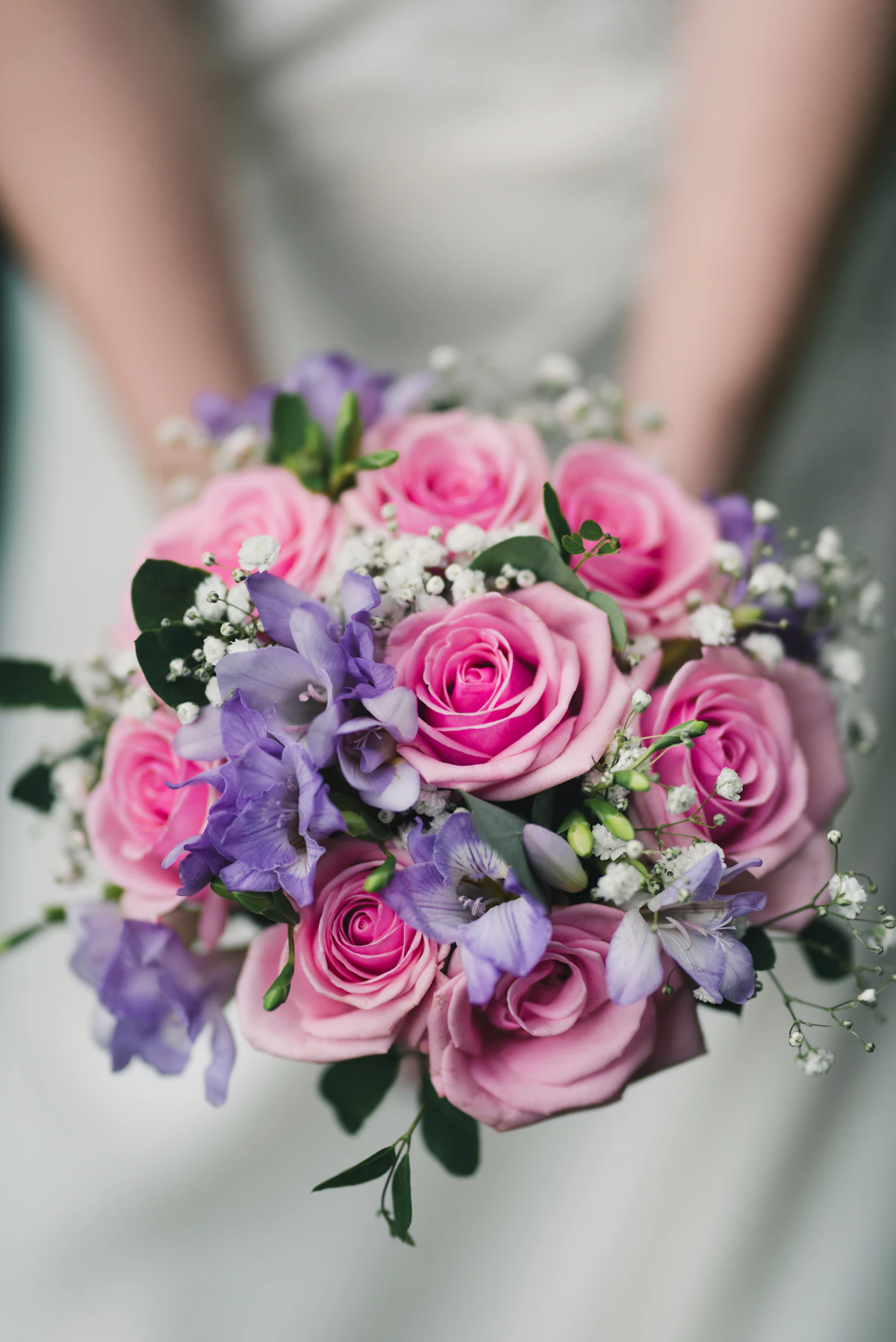 A bouquet of pink roses and purple freesias with baby's breath